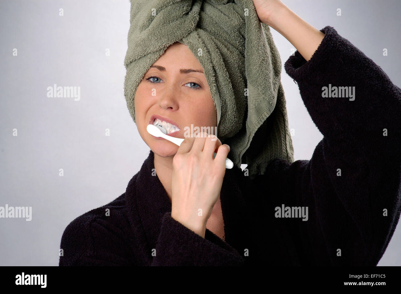 Giovane donna, età 20-25, spazzolare i suoi denti, tenendo verde sulla sua testa, vestita di nero accappatoio. Foto Stock