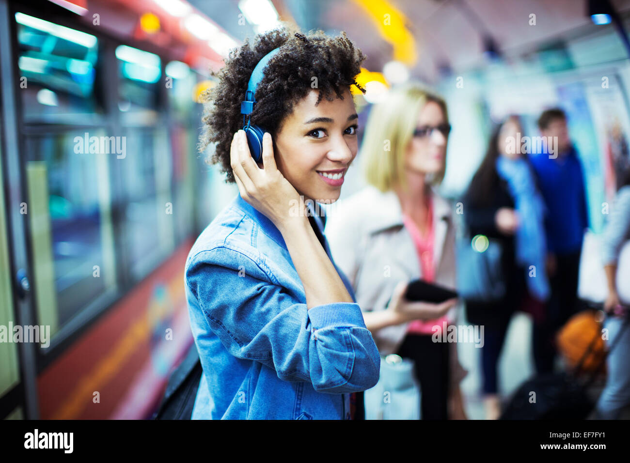 Donna sorridente ascoltando le cuffie in metropolitana Foto Stock