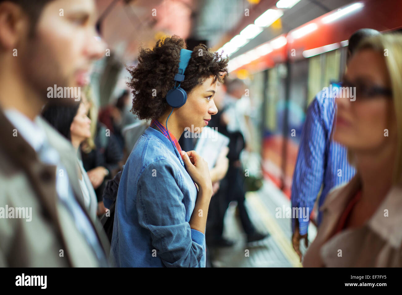Donna ascoltando le cuffie in una stazione ferroviaria Foto Stock