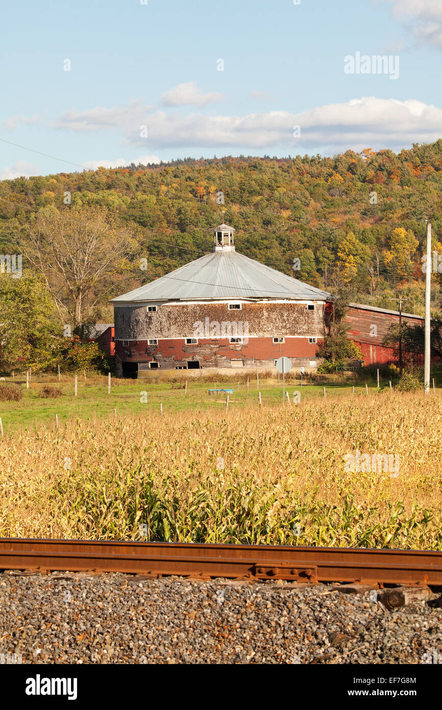 Round dairy barn in una fattoria nel nord del Vermont negli Stati Uniti d'America. I binari della ferrovia in primo piano. L'autunno. Foto Stock