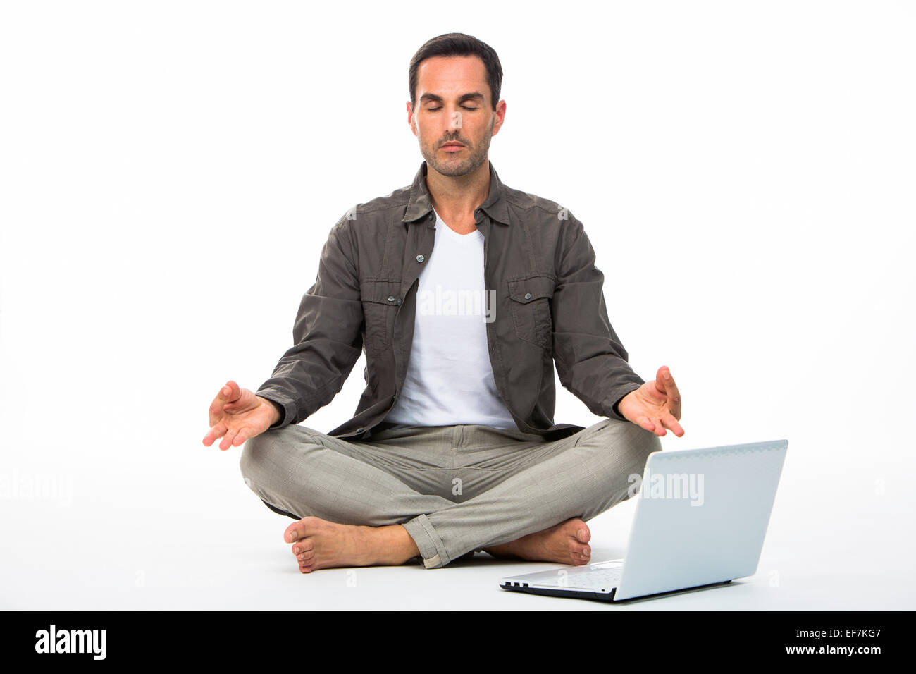 L'uomo sitted sul pavimento con gli occhi chiusi la pratica dello yoga con computer portatile accanto a lui Foto Stock