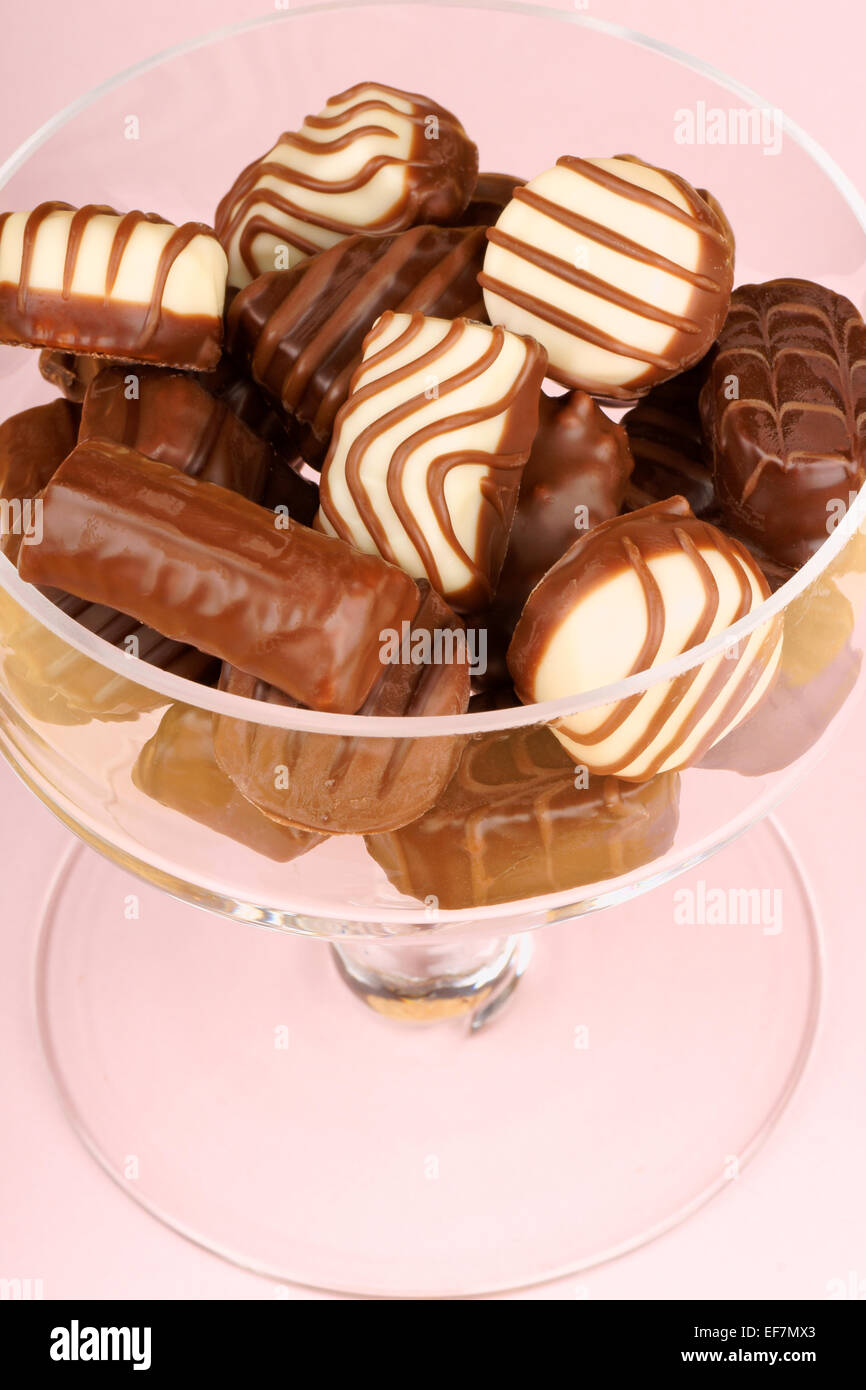 Praline di cioccolato assortimento in una ciotola di vetro su uno sfondo rosa Foto Stock