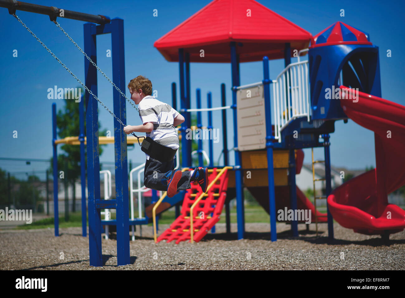 Ragazzo (10-11) oscillanti su swing sul parco giochi Foto Stock