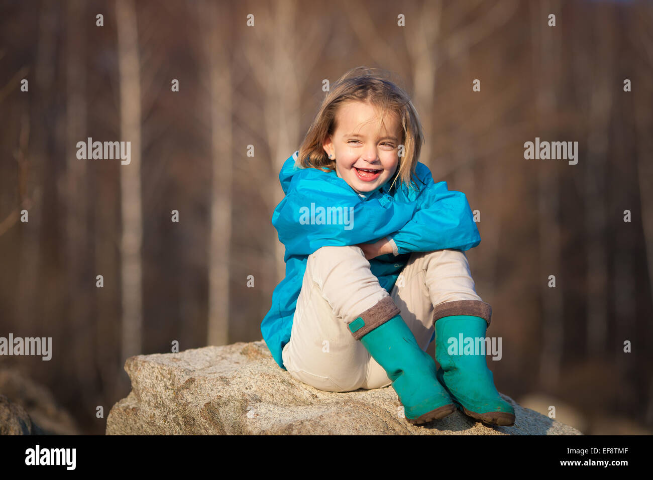 La ragazza (4-5) seduto su roccia, sorridente Foto Stock