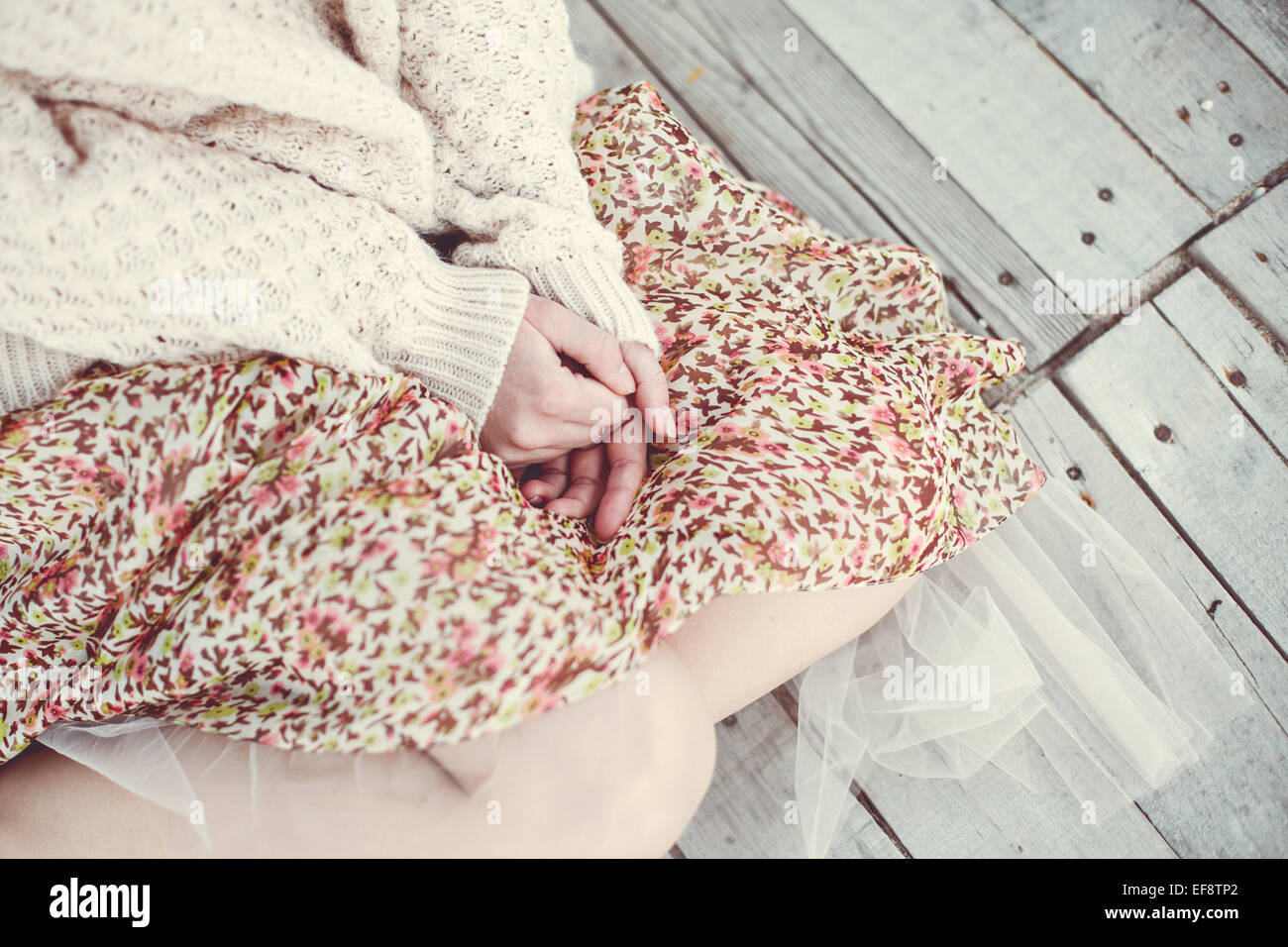 Metà vista in sezione della ragazza seduta sul pavimento in legno all'esterno ed indossare gonna e maglione Foto Stock