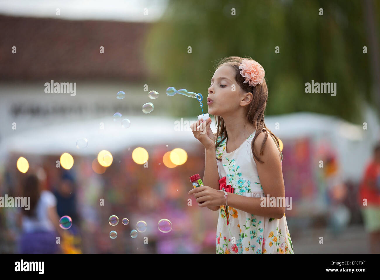 La ragazza (8-9) nel vestire soffiando bolle di sapone Foto Stock