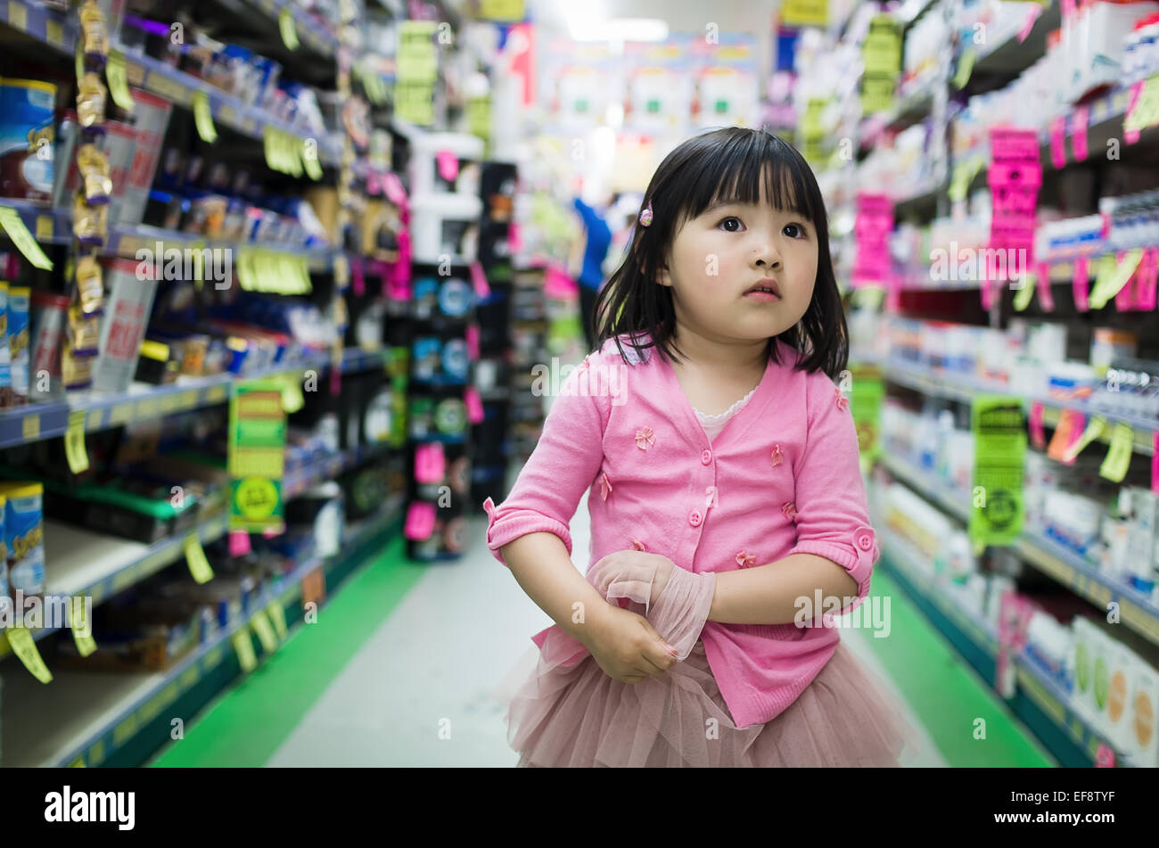 Vista frontale della piccola ragazza camminare da solo tra bancarelle nel supermercato Foto Stock