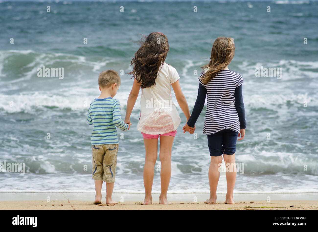 La Bulgaria, due ragazze (8-9) e ragazzo (4-5) a piedi dalla linea surf tenendo le mani guardando il mare Foto Stock