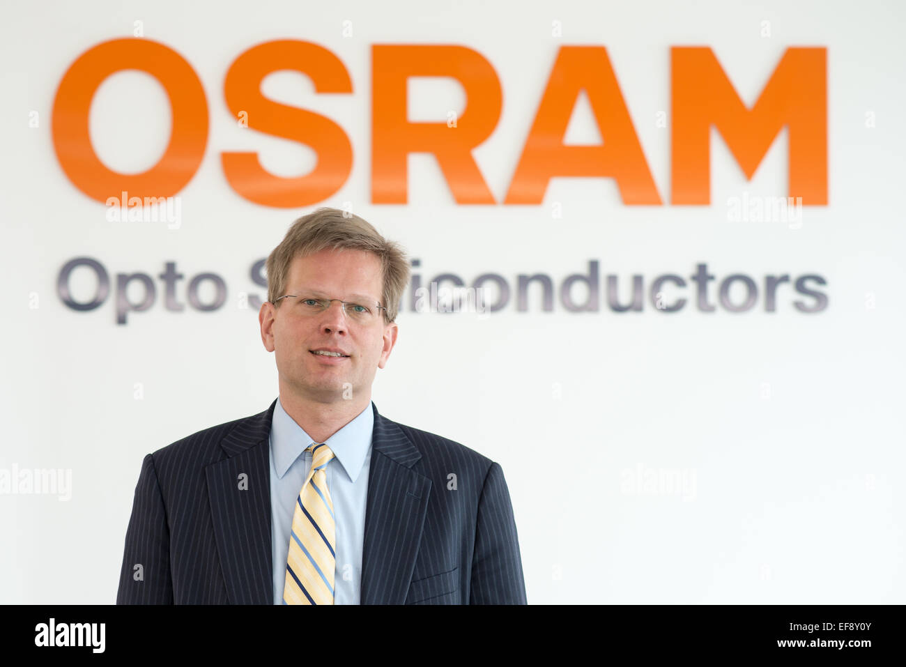 Il CEO del produttore di semiconduttori Osram Opto, Aldo Kamper, stand con bracci ripiegati nella parte anteriore del logo aziendale presso la Osram impianto di produzione in Regensburg, Germania, 26 gennaio 2015. Foto: Armin Weigel/dpa Foto Stock