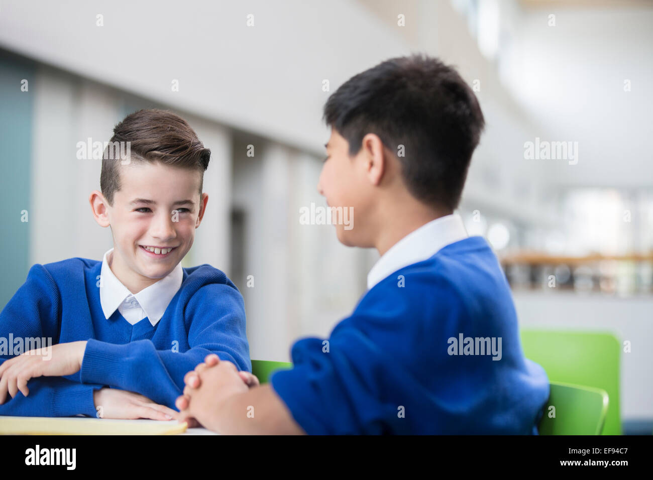 Due scolari sorridenti indossano uniformi scolastiche parlando al banco in aula Foto Stock