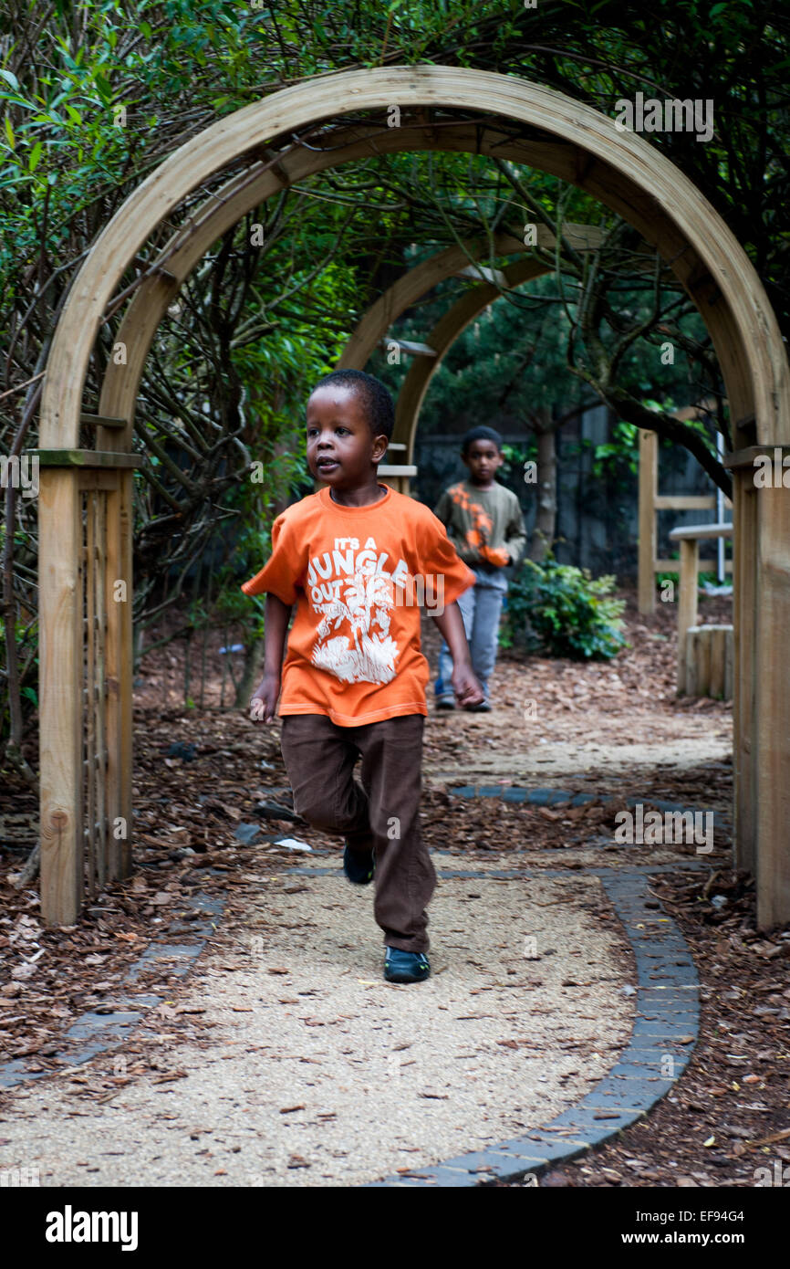 Sorridenti dei bambini che giocano nel parco giochi del giardino della scuola primaria in London W2 Foto Stock