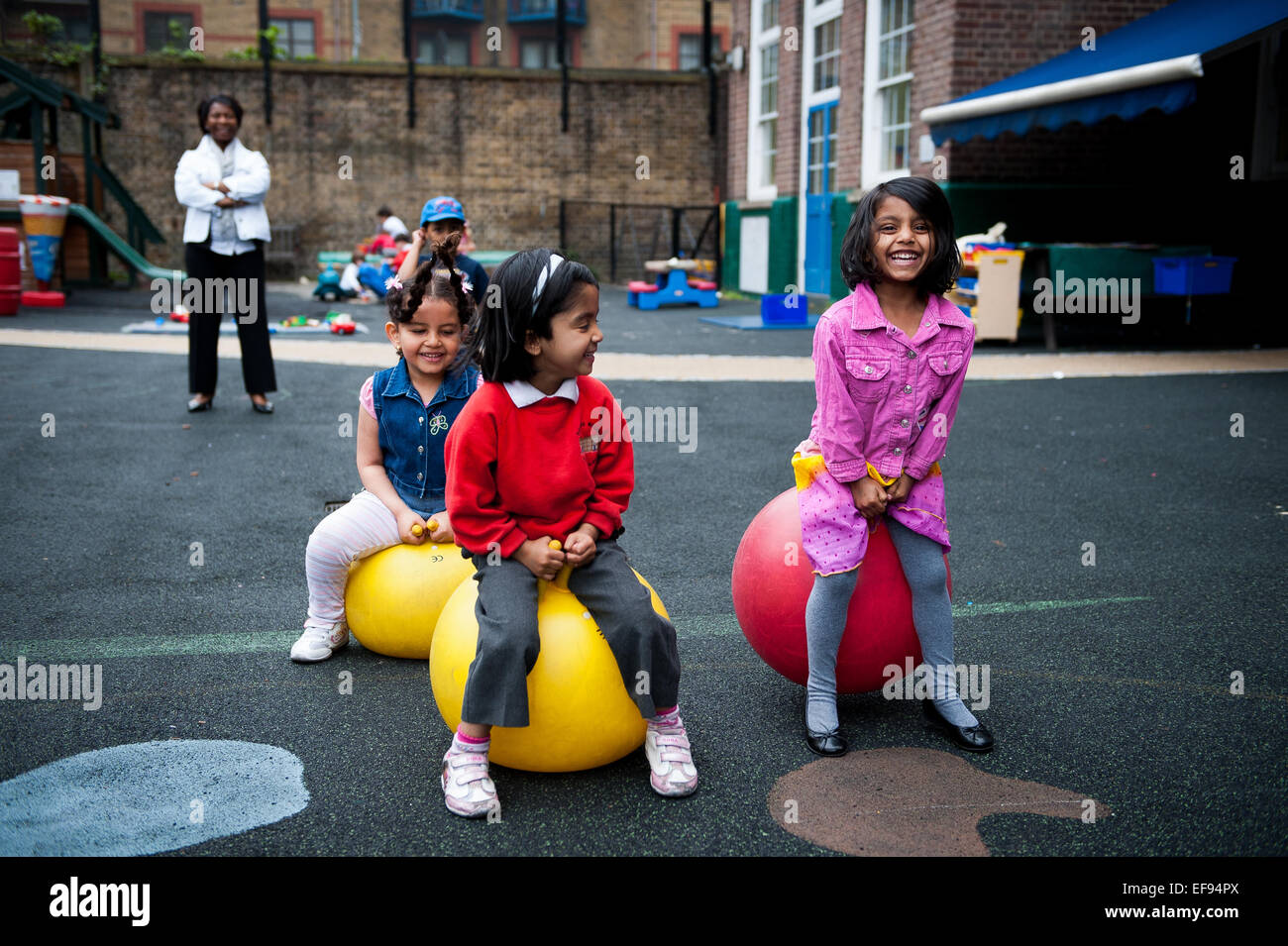 Ragazze rimbalzare sul Spacehoppers nel parco giochi della scuola primaria in London W2 Foto Stock