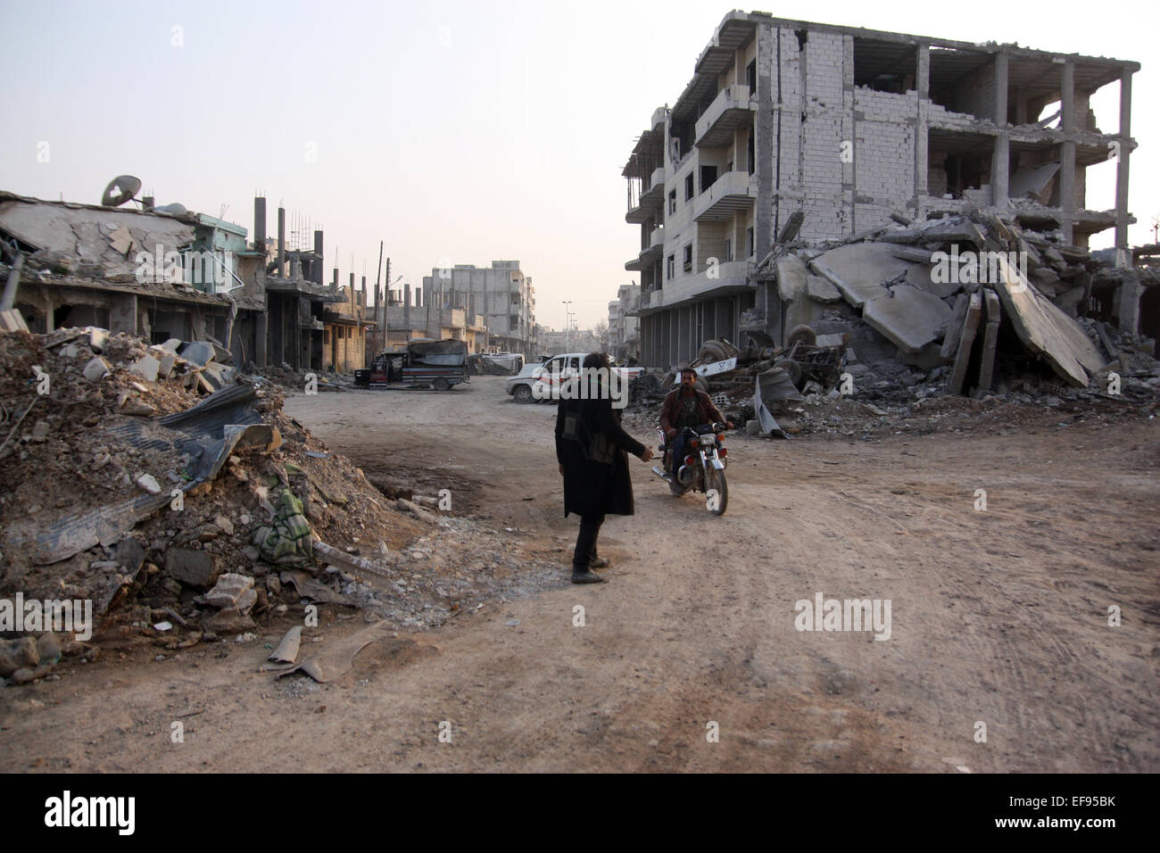 Due uomini stand in una strada deserta tra distrutte auto, le case e le macerie che dominano il scenerey nella città di Kobane, Siria, 28 gennaio 2015. Combattenti curdi sono riusciti a spingere indietro le forze del cosiddetto è stato islamico, dalla città di Kobane. Razzi e azioni di combattimento, tuttavia, hanno ucciso molti civili e sinistra Kobane completamente devastata. Foto: Jan Kuhlmann/dpa Foto Stock