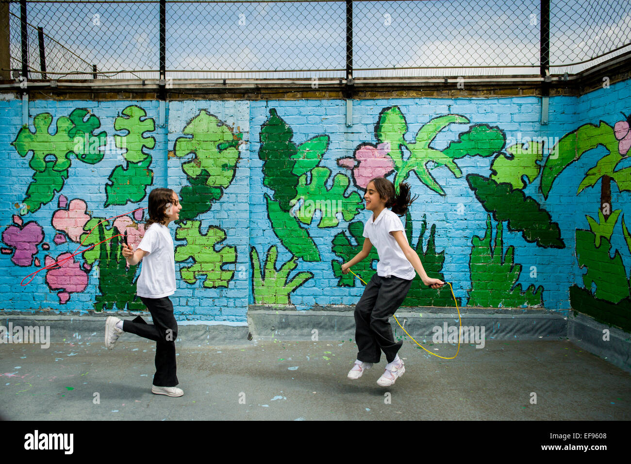 2 ragazze saltando in graffiti parco giochi a scuola Foto Stock