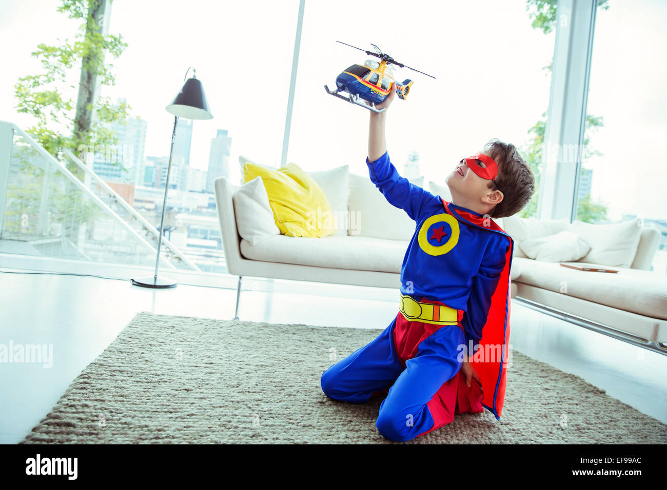 Il supereroe ragazzo giocando con elicottero giocattolo in salotto Foto Stock