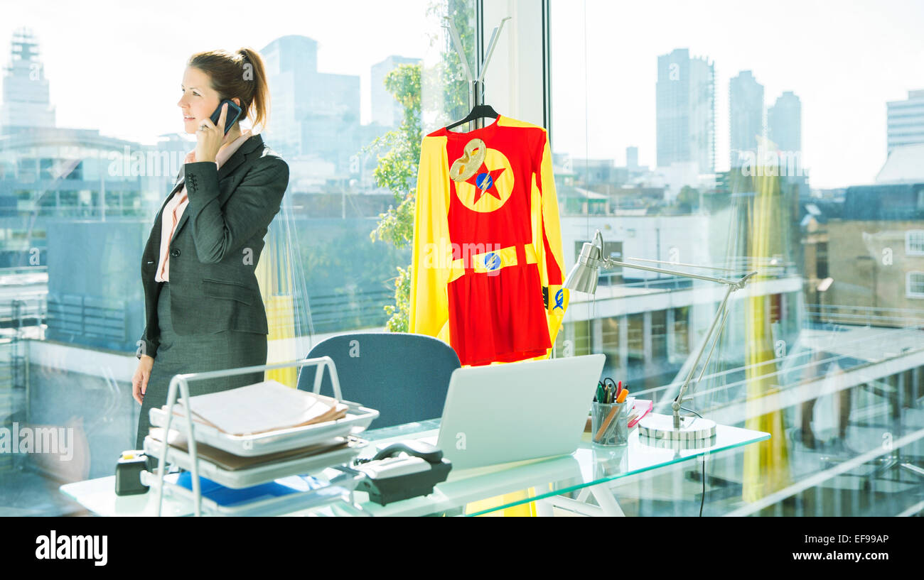 Imprenditrice parlando al cellulare con il costume da supereroe dietro di lei Foto Stock