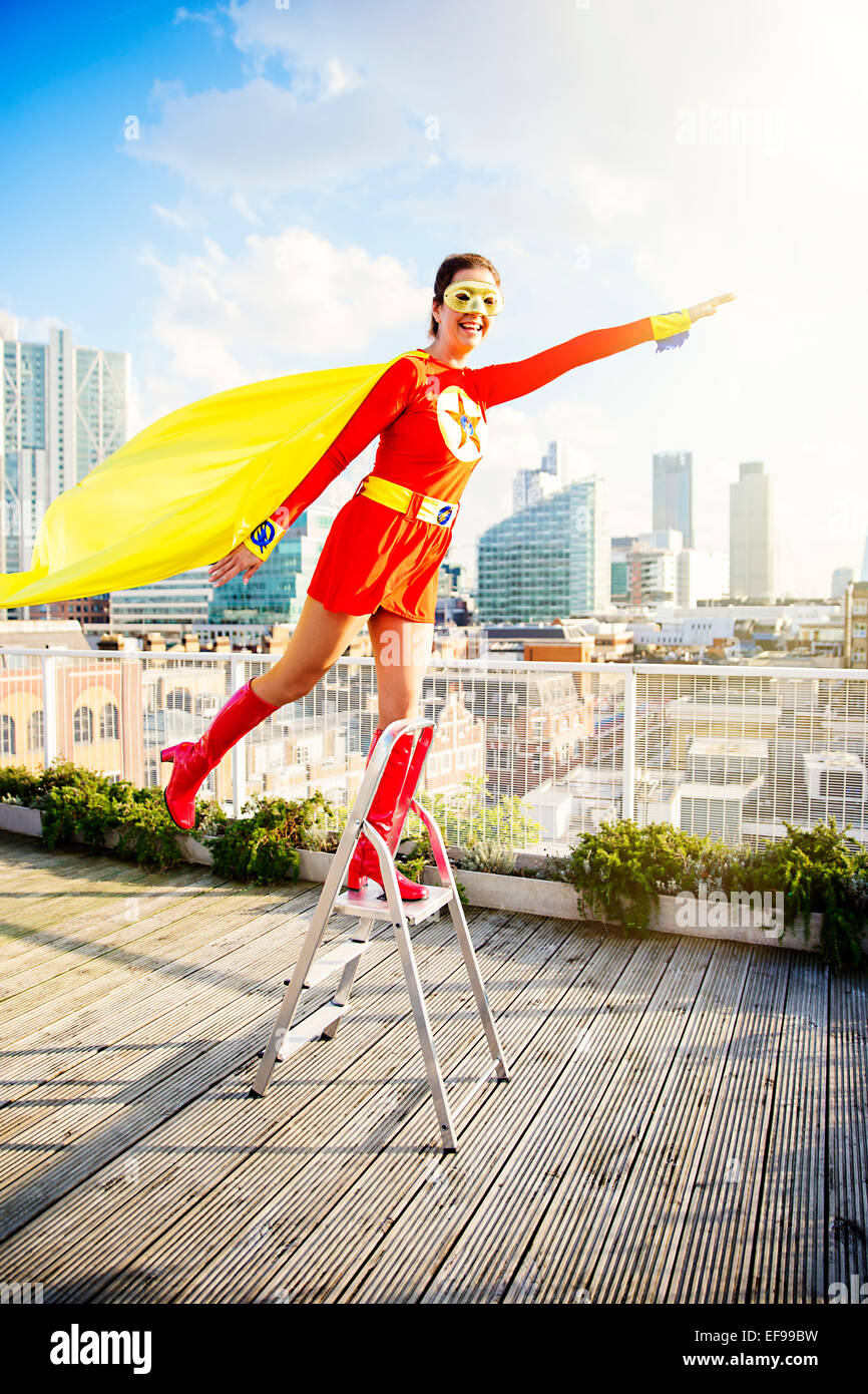 Il supereroe che stando in piedi sulla scala sul tetto della città Foto Stock
