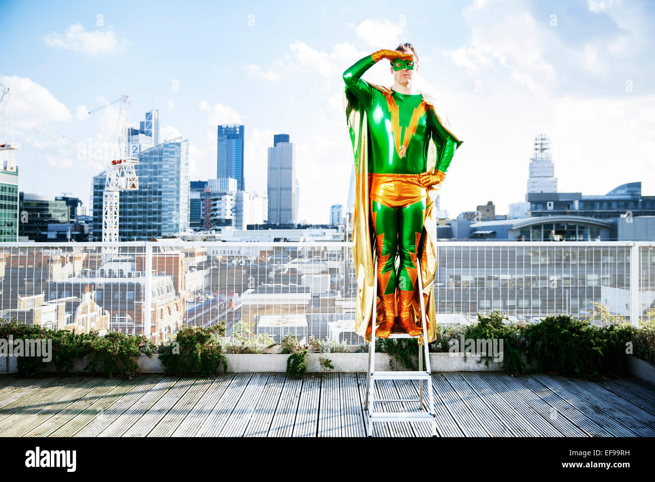 Il supereroe che si affaccia su vista dalla scala sul tetto della città Foto Stock