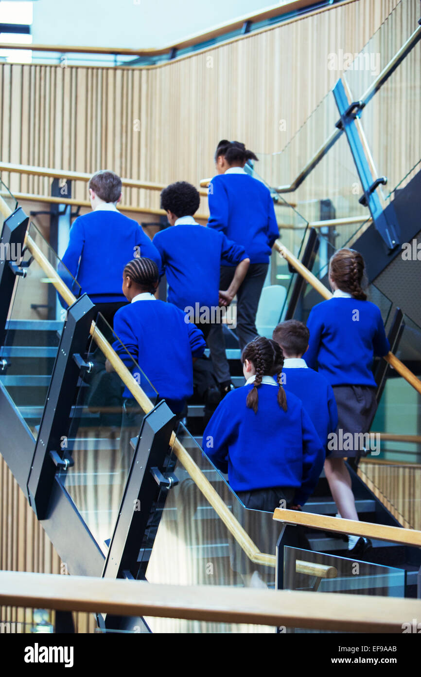 Vista posteriore di un gruppo di alunni blu che indossano uniformi scolastiche salendo le scale nella scuola Foto Stock