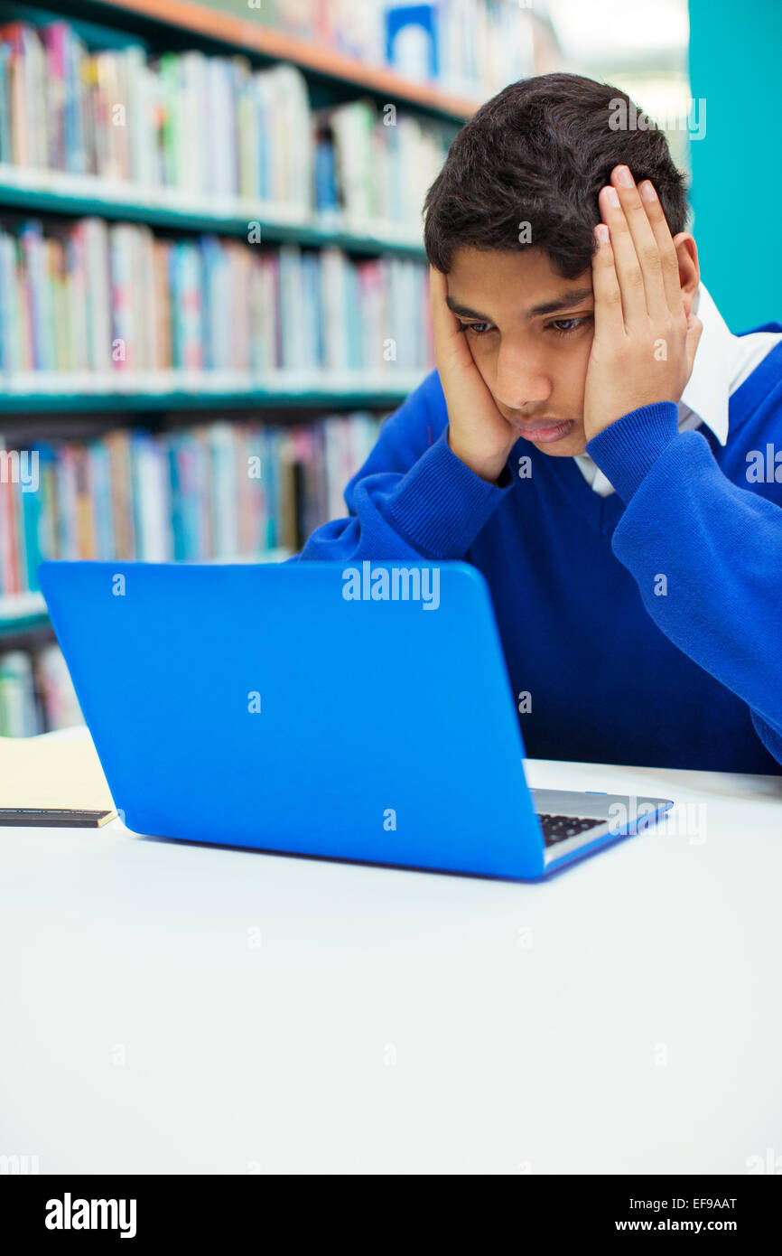 Ritratto di preoccupato studente cerca sul computer portatile in biblioteca Foto Stock