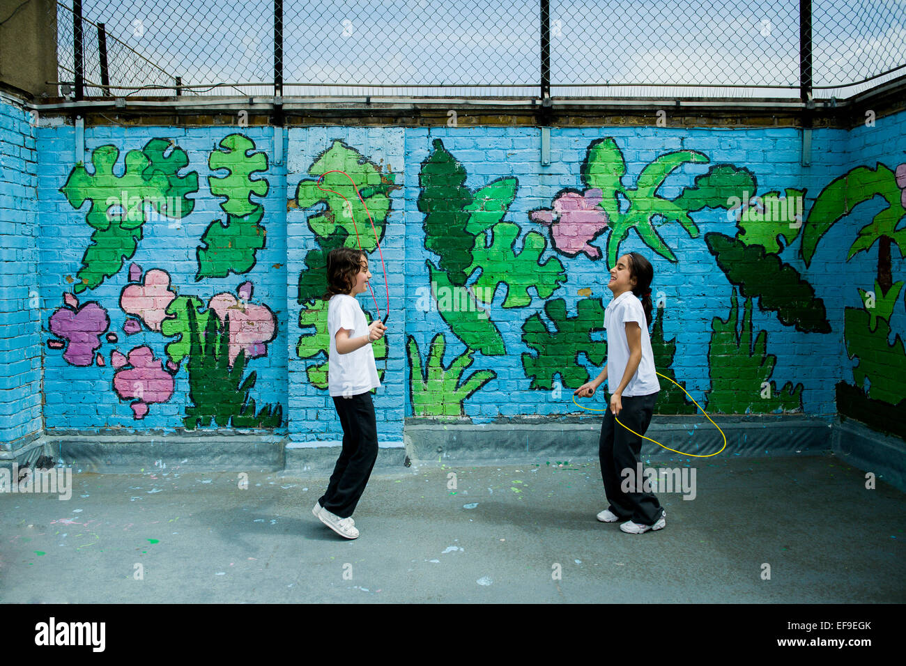 2 ragazze della scuola saltando nel parco giochi sul tetto al loro interno della città la scuola primaria con i graffiti sulla parete dietro Foto Stock