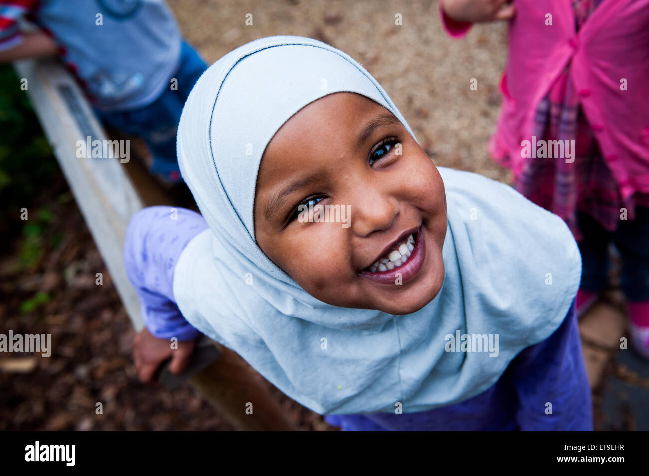 Sorridenti ragazzina musulmana in hijab velo nel parco giochi della scuola primaria in London W2 Foto Stock