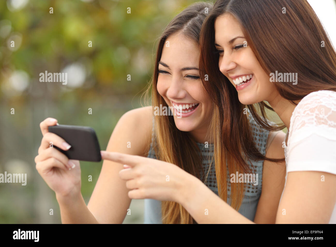 Due donne divertenti amici di ridere e di condivisione sociale dei media video in uno smart phone all'aperto Foto Stock