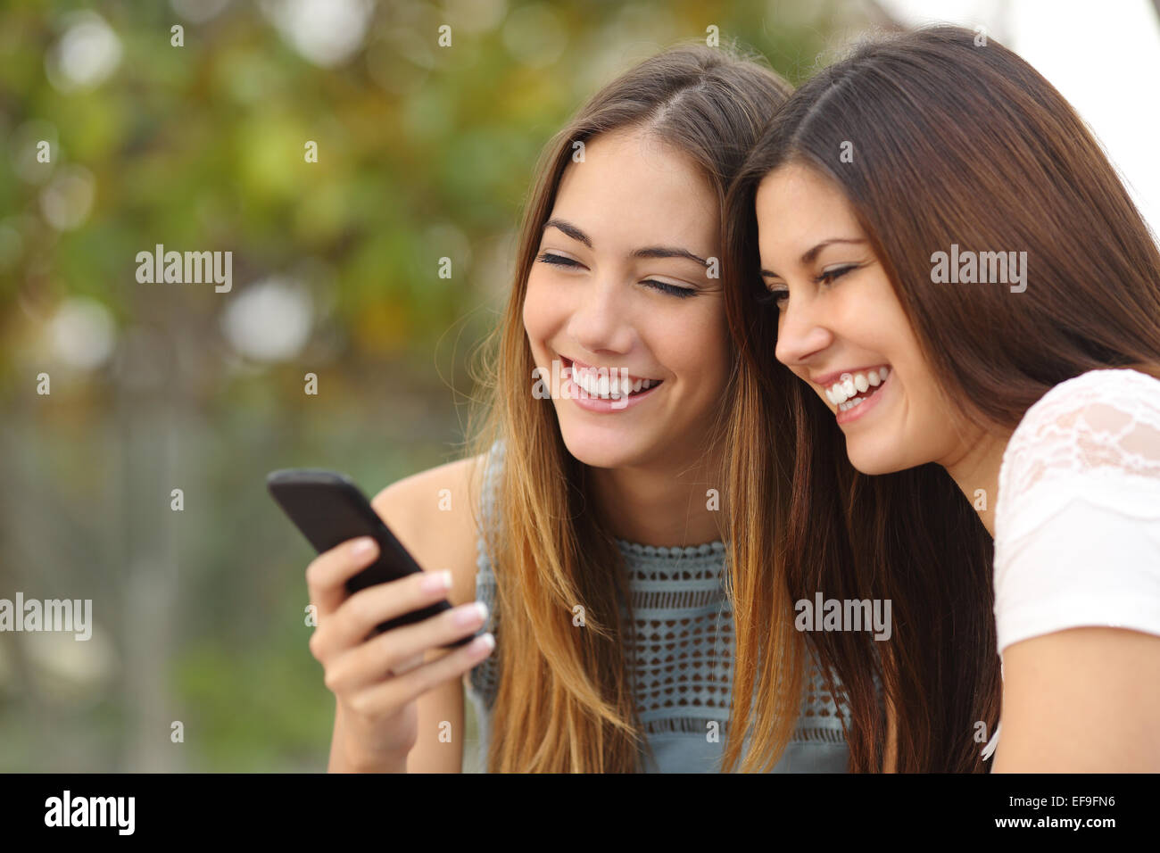 Due felici donne amici di condivisione sociale dei media in uno smart phone all'aperto in un parco Foto Stock