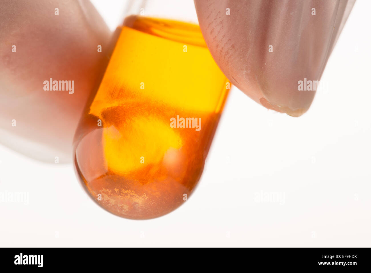 Incandescente liquido arancione in provetta vicino, detenute da dita. Foto Stock