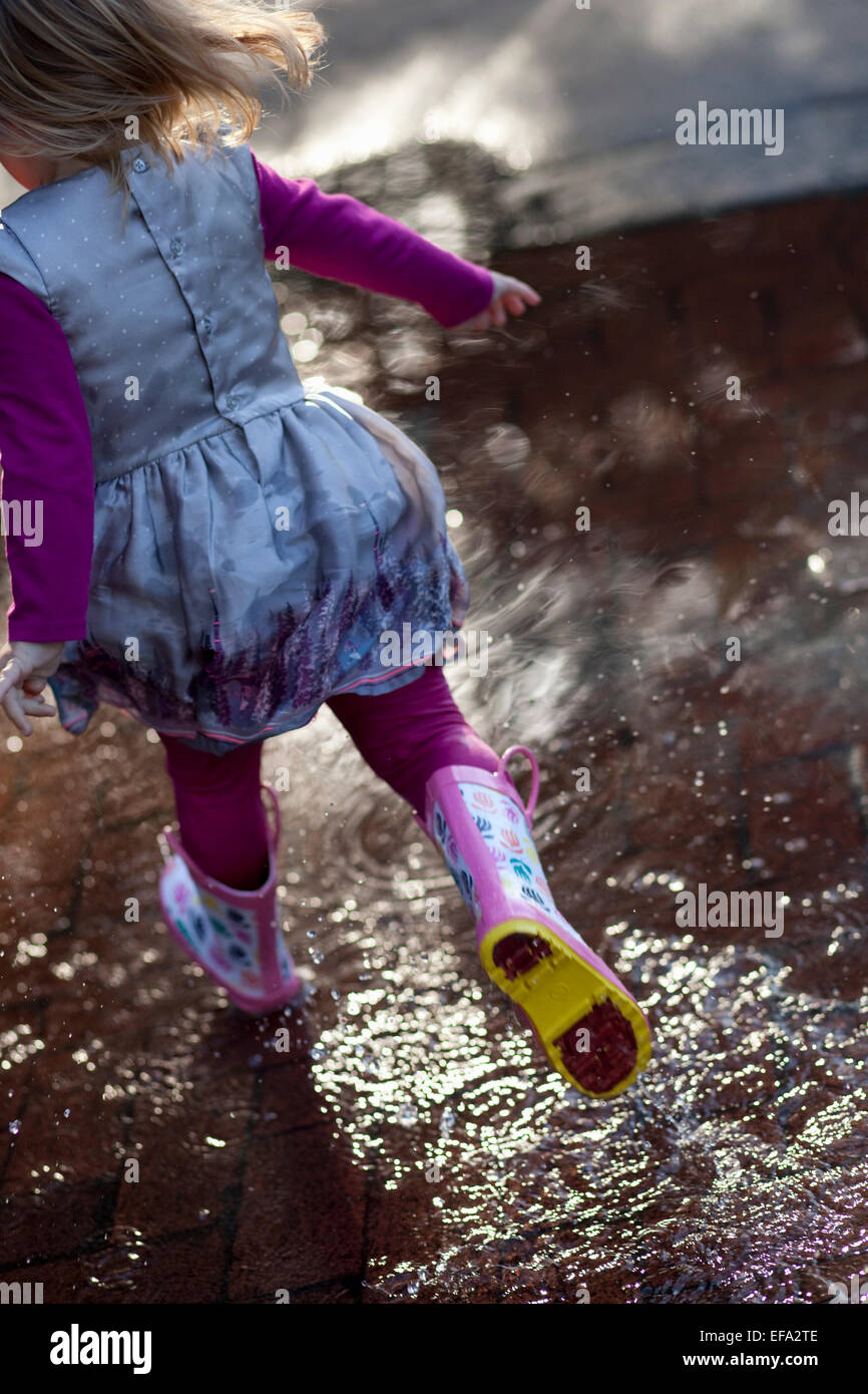 Un po' ragazza indossare stivali da pioggia corre attraverso una pozzanghera. Foto Stock