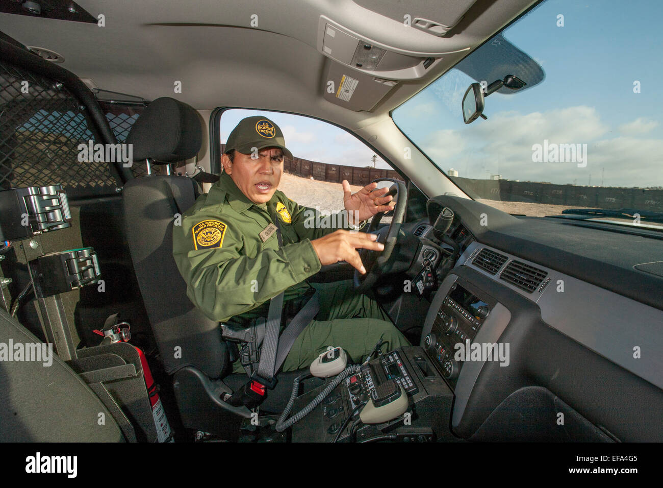 Polizia della "Bunker Hill' area dell'U.S./Messico Confine vicino Tijuana, una frontiera ispanica ufficiale di pattuglia nel suo SUV colloqui sulla sua radio con la sede centrale. La Pattuglia di Confine è parte dell'U.S. Department of Homeland Security. Nota recinzione di confine in background. Foto Stock