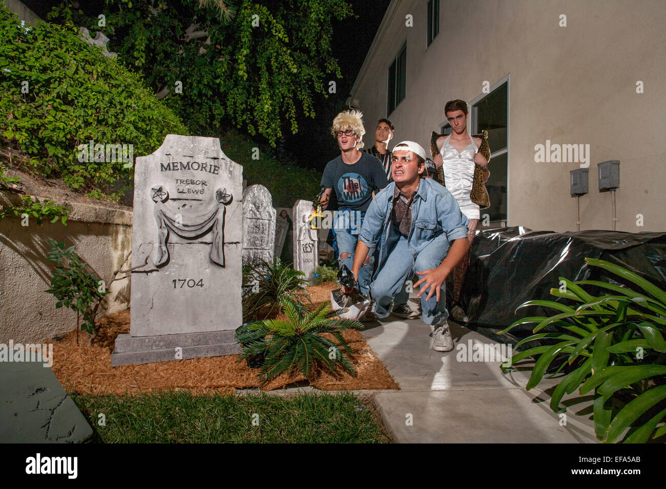 Opportunamente indossare costumi festosa, quattro giovani uomini entrare nello spirito di una notte di Halloween "Haunted Mansion's" fake headstone in Lake Forest, CA. Foto Stock