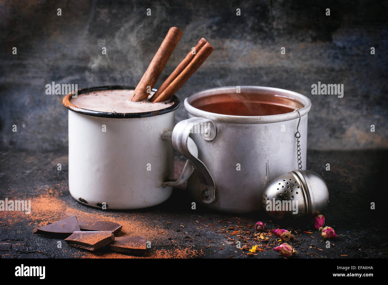 Due tazze vintage con tè e cioccolata calda servita a secco con tè, boccioli di rosa, il cioccolato tritato e bastoncini di cannella sul nero ba Foto Stock