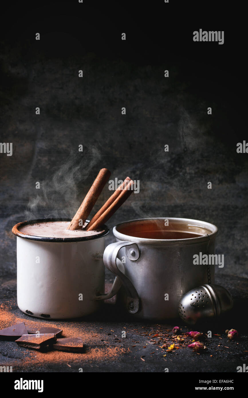 Due tazze vintage con tè e cioccolata calda servita a secco con tè, boccioli di rosa, il cioccolato tritato e bastoncini di cannella sul nero ba Foto Stock