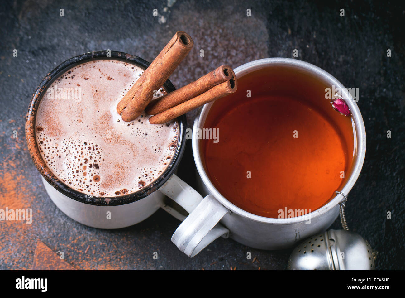 Due tazze vintage con tè e cioccolata calda servita a secco con tè, boccioli di rosa, il cioccolato tritato e bastoncini di cannella sul nero ba Foto Stock