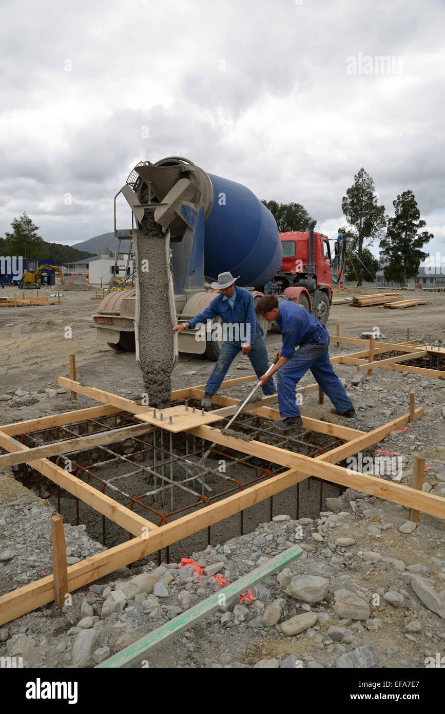 Un team di costruttori dirige il calcestruzzo bagnato da un camion di cemento nelle fondamenta di un edificio di grandi dimensioni Foto Stock