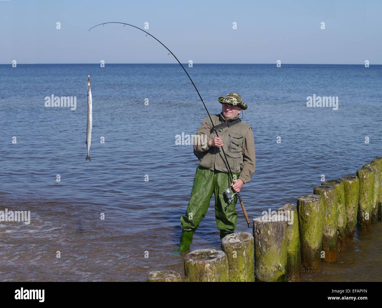 L'uomo con il pesce e la canna da pesca sul mare sullo sfondo Foto Stock