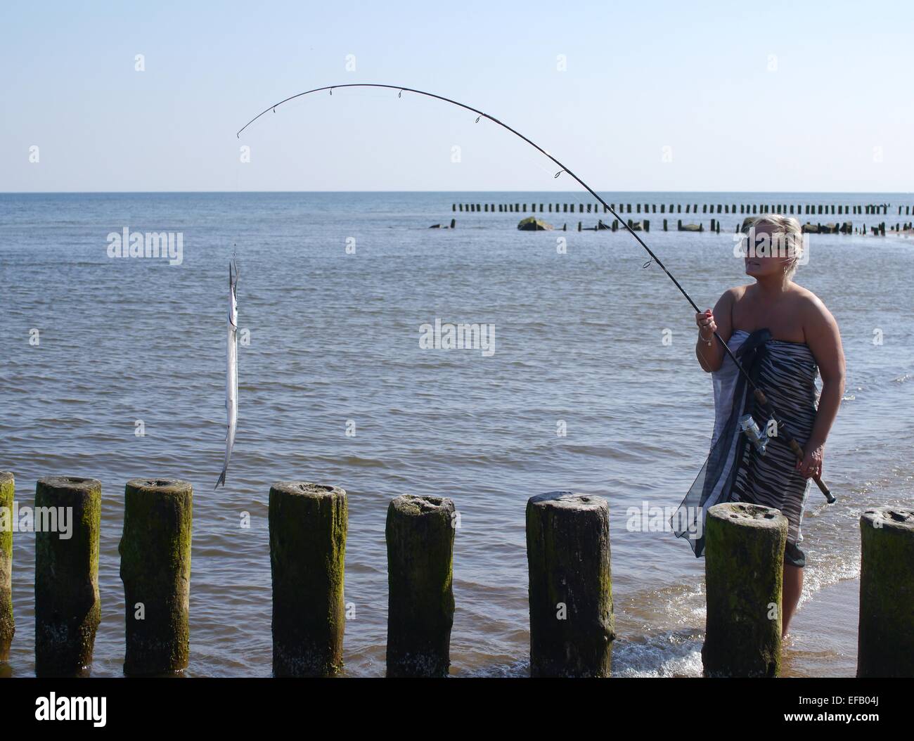 Donna con il pesce e la canna da pesca sul mare sullo sfondo Foto Stock