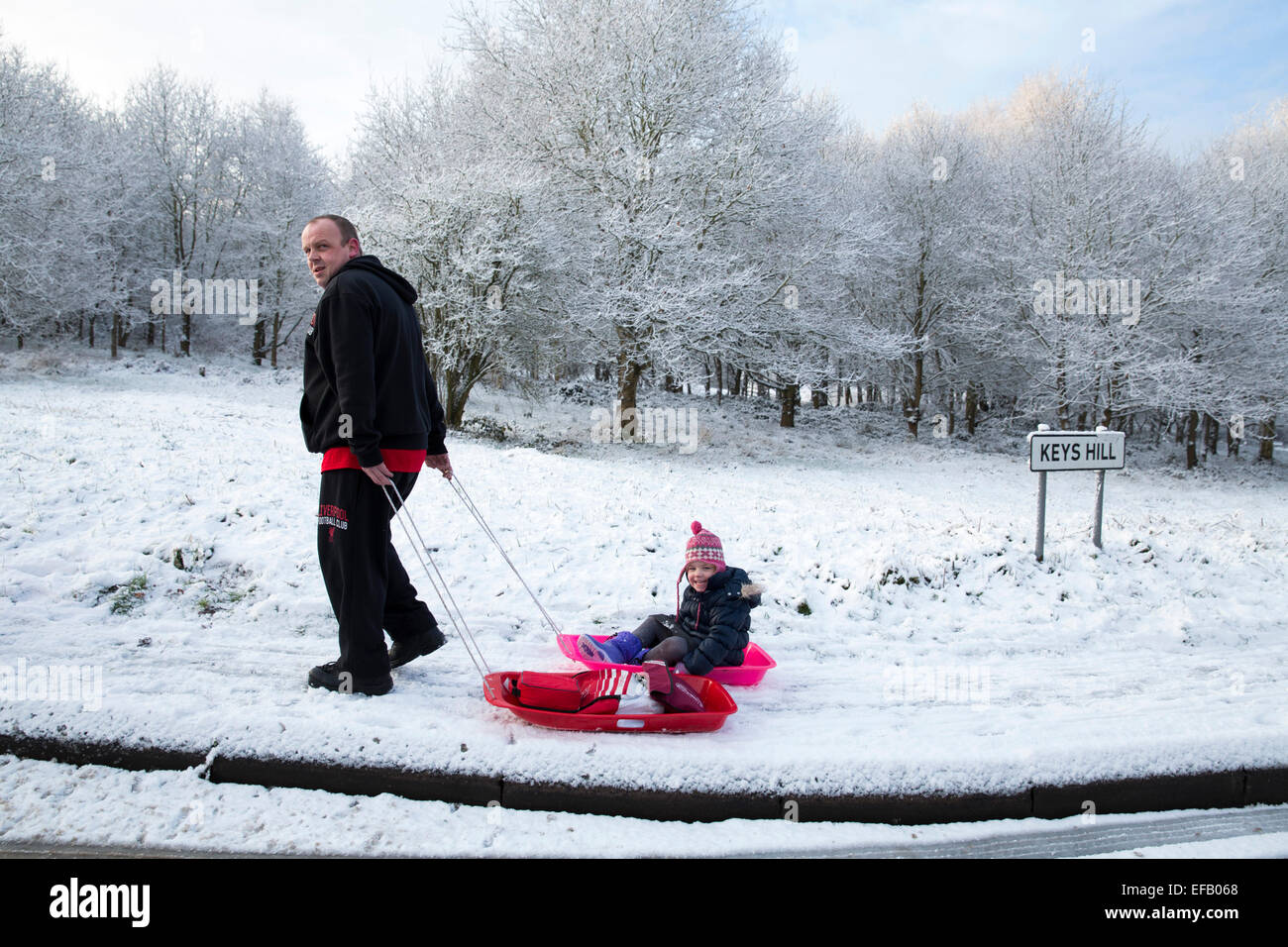 Coperta di neve baddesley ensor nel nord Warwickshire, Regno Unito. Un bambino è sledged a scuola lungo la collina di chiavi da un adulto Foto Stock