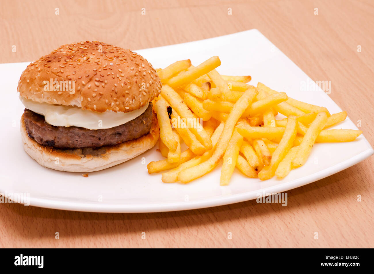 Hamburger e uova fritte in un seme di sesamo Bun con chip su una piastra bianca Foto Stock