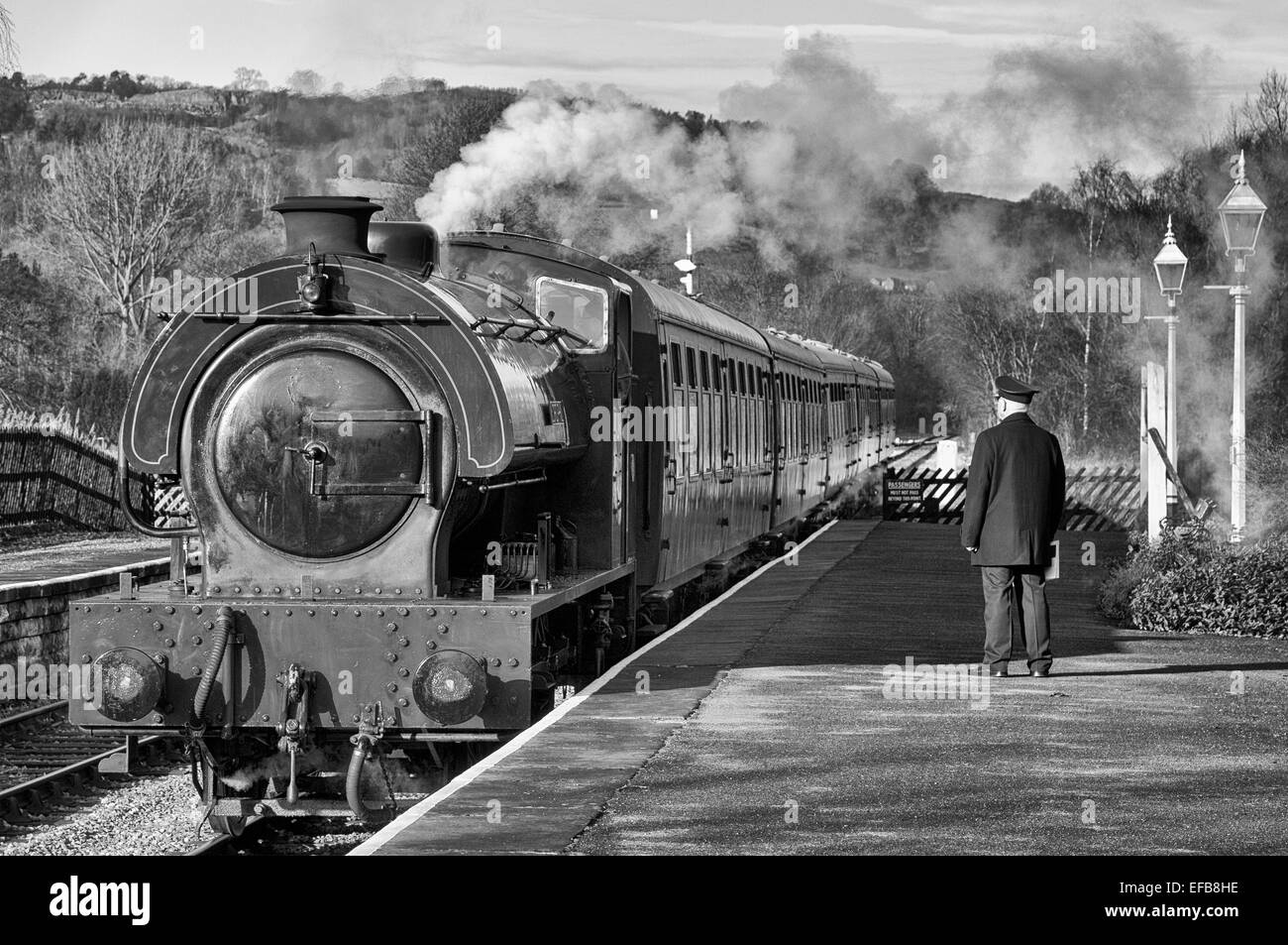 Master in bianco e nero in attesa sulla piattaforma della stazione ferroviaria di Darley Dale mentre un treno passeggeri arriva tipico degli anni '40, '50 e '60 Foto Stock