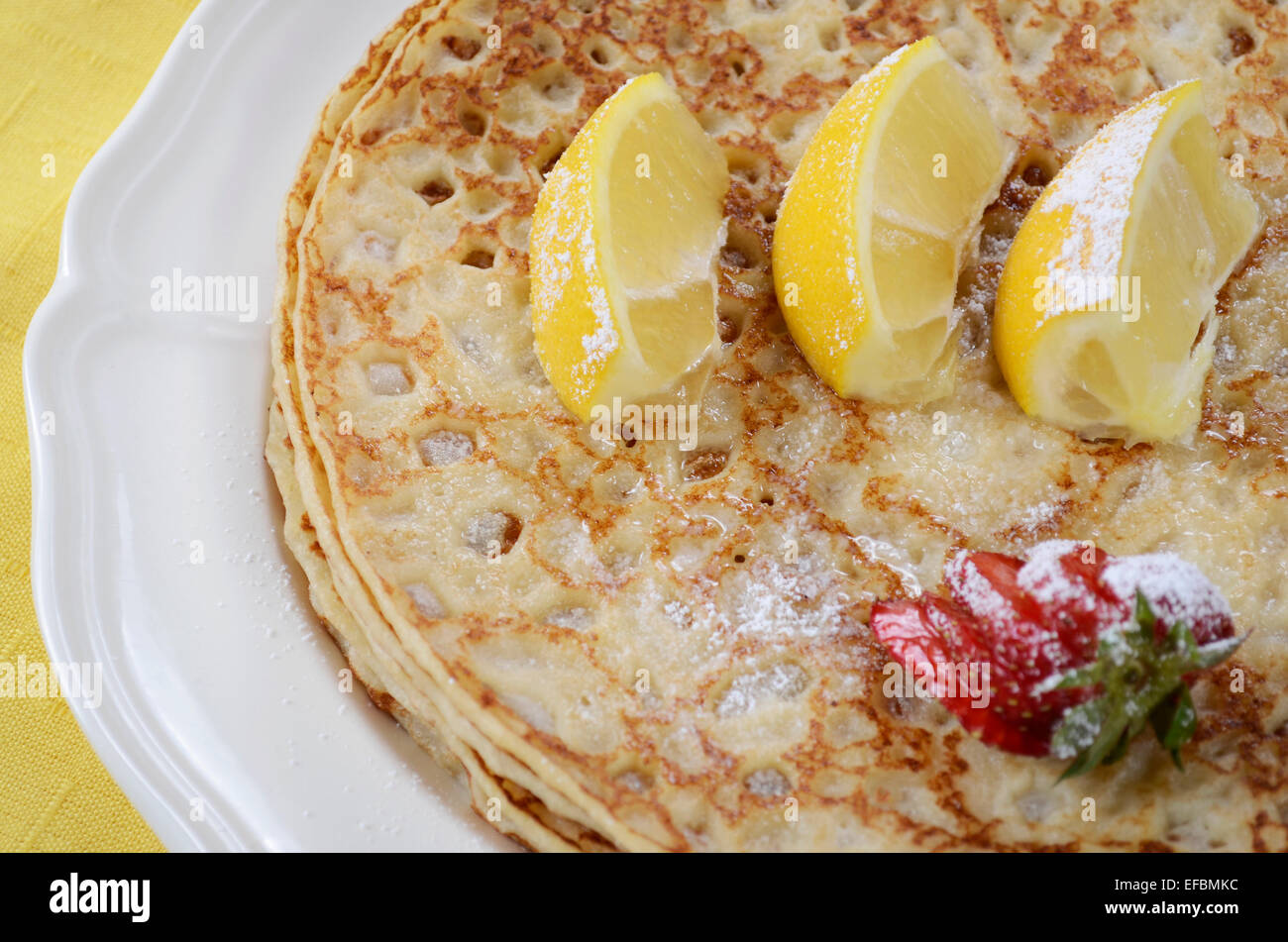 Martedì grasso Martedì Pancake pancake con limoni e fragole con i colori giallo e blu di tovaglioli su bianco vintage shabby chic tavolo. Foto Stock