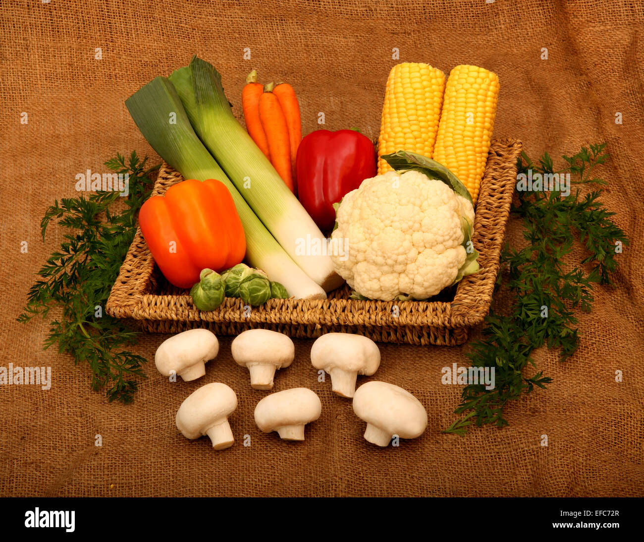 Un vassoio di vimini contenenti una varietà di verdure con foglie di carota accanto al vassoio, tutti su di un panno di tela Foto Stock
