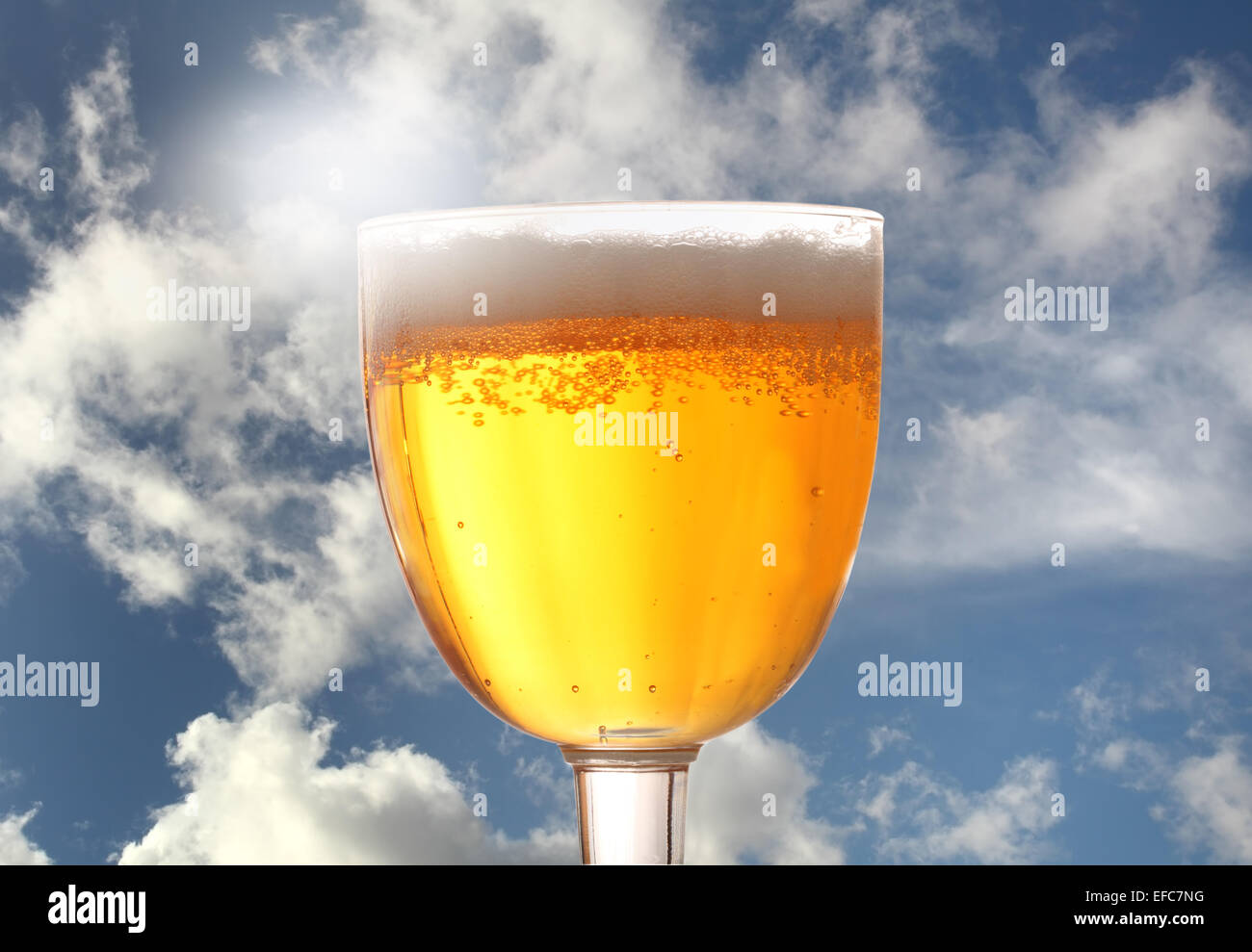 Un bicchiere di birra contro un soleggiato cielo blu con nuvole di luce Foto Stock