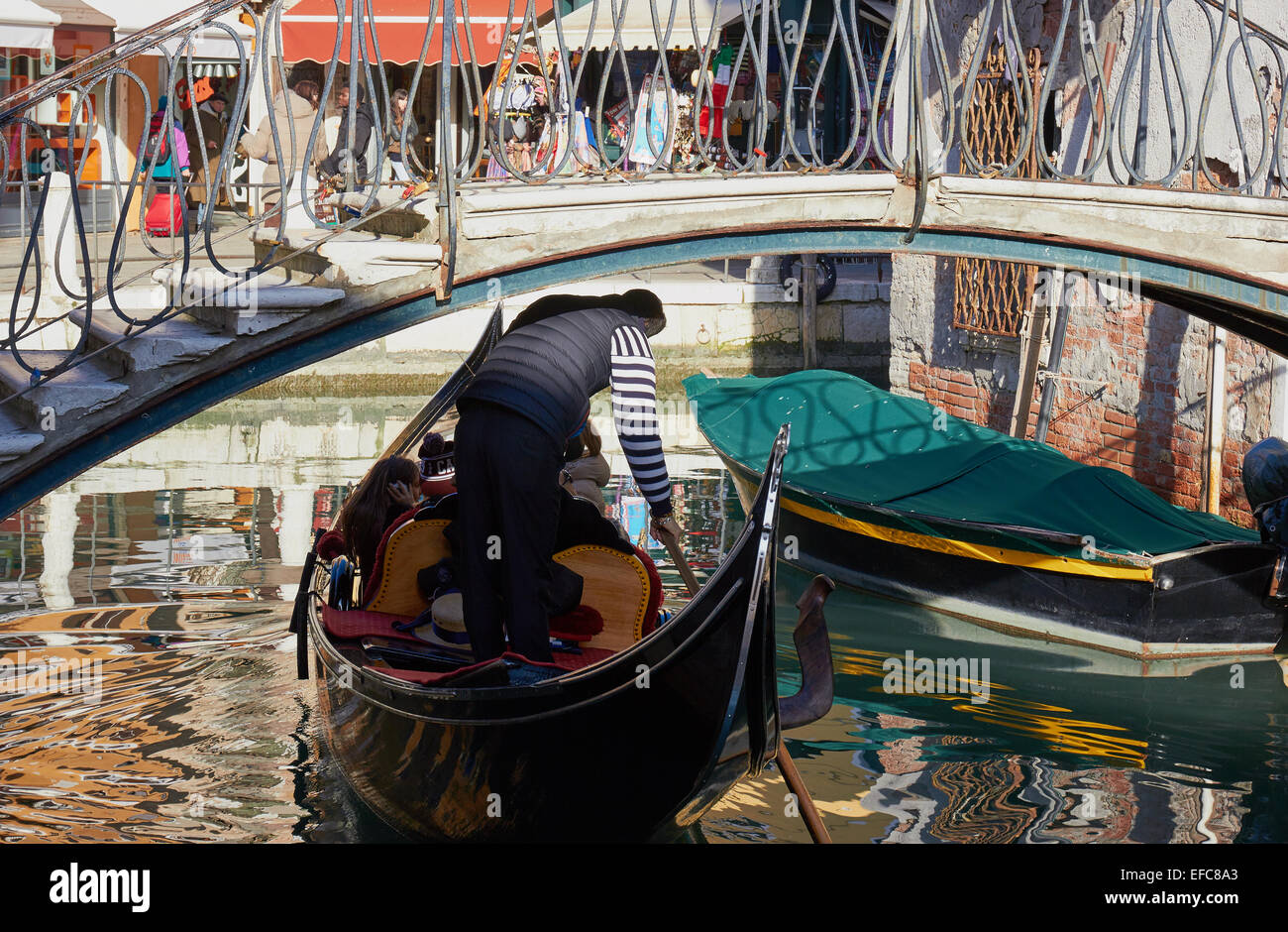 Gondoliere anatre come egli righe la sua gondola sotto un piccolo ponte sul canale di Venezia Veneto Italia Europa Foto Stock