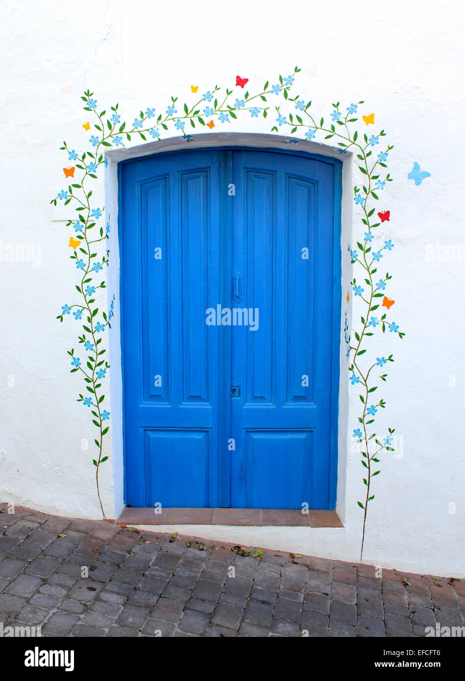 Un dipinto luminosamente porta blu decorato con il murale di un fronte di piante e fiori su di una parete dipinta di bianco Foto Stock