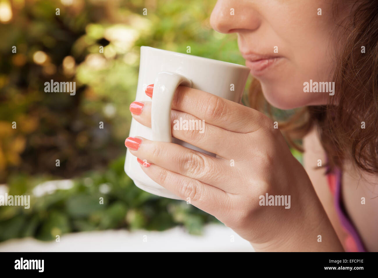 Donna sorridente detiene white tazza di caffè nelle sue mani. Primo piano in stile vintage foto all'aperto Foto Stock