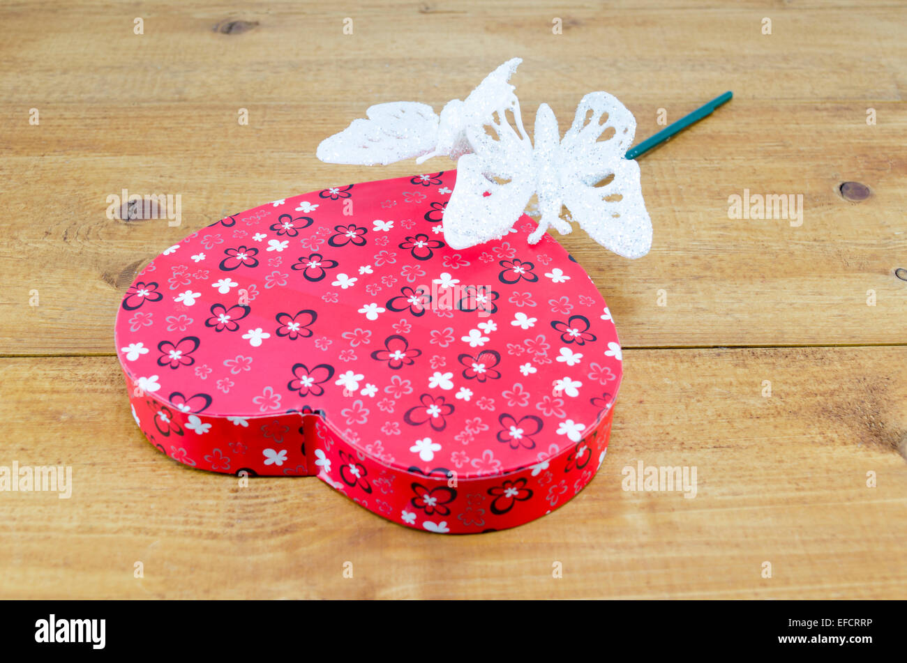 A forma di cuore e la scatola a farfalla a forma di bacchetta magica su una tavola di legno Foto Stock