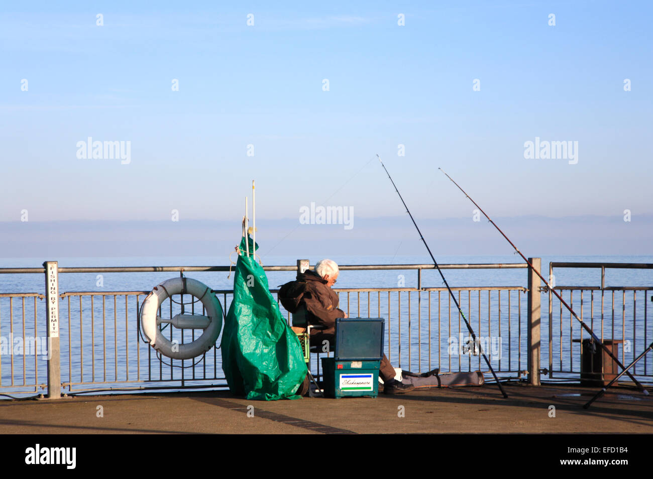 Un senior citizen pesca marittima al fine di Southwold Pier, Suffolk, Inghilterra, Regno Unito. Foto Stock