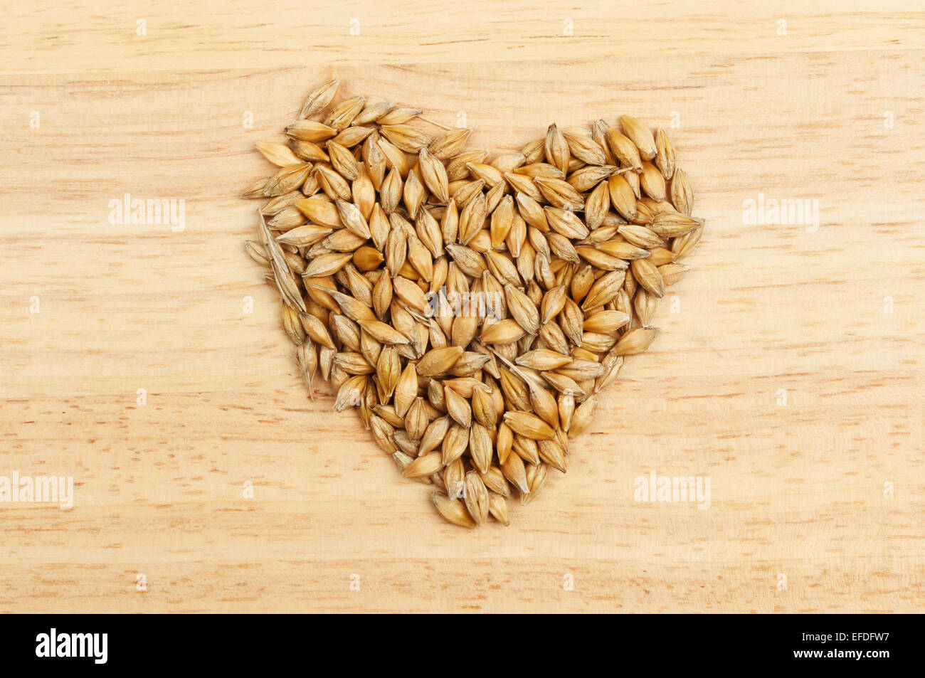 Chicchi d'orzo a forma di cuore su una tavola di legno Foto Stock